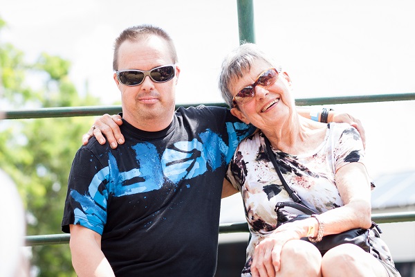 man with sunglasses and older woman with sunglasses smiling sitting outside with arms around each other